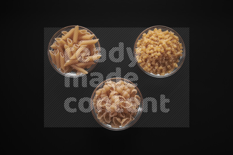 Different pasta types in glass bowls on black background