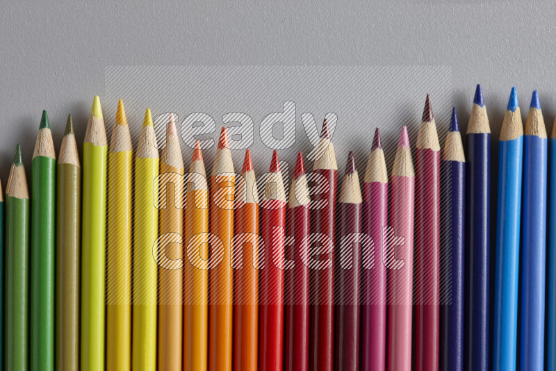 A collection of colored pencils arranged showcasing a gradient of different hues on grey background