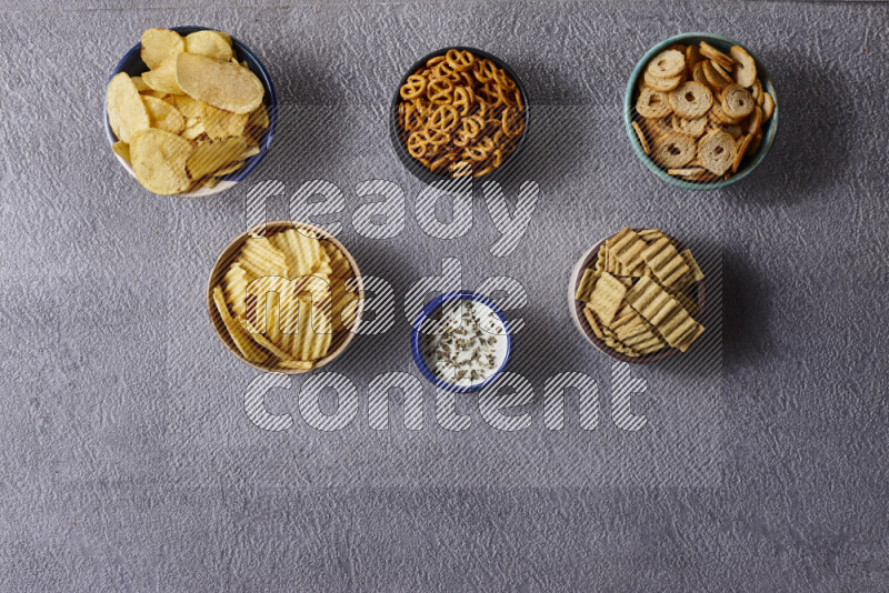 Assorted snacks in pottery bowls on grey background