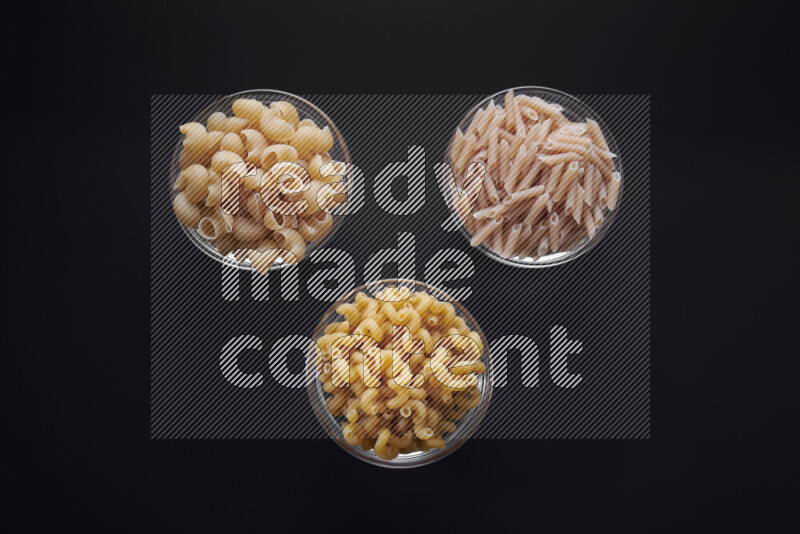 Different pasta types in glass bowls on black background
