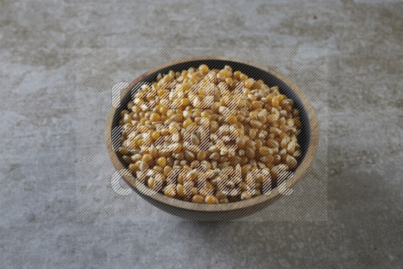 corn kernel in a wooden bowl on a grey textured countertop