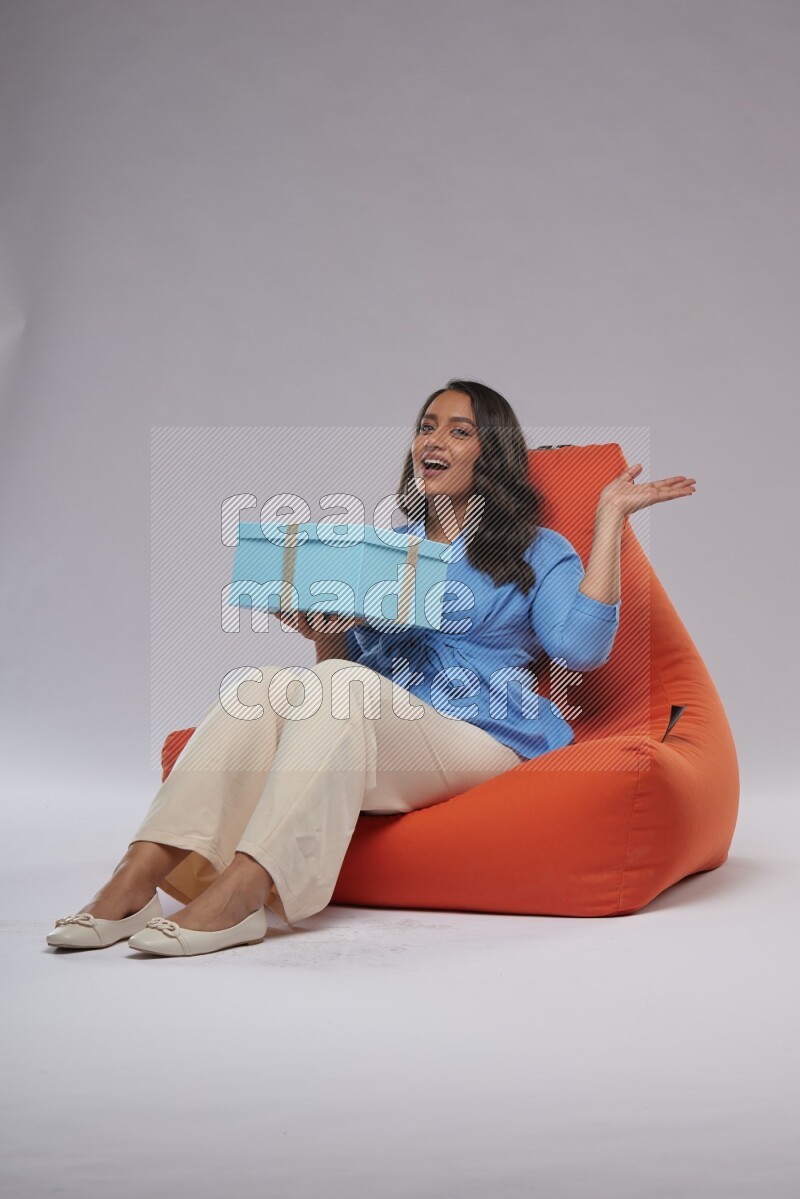 A woman sitting on an orange beanbag and opining a gift