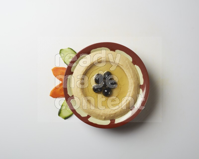 Hummus in a traditional plate garnished with black olives on a white background