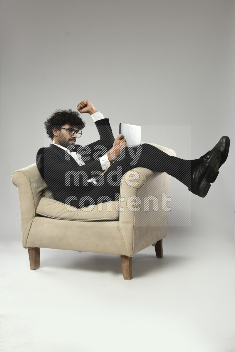 A man wearing formal sitting on a chair gaming on a tablet on white background