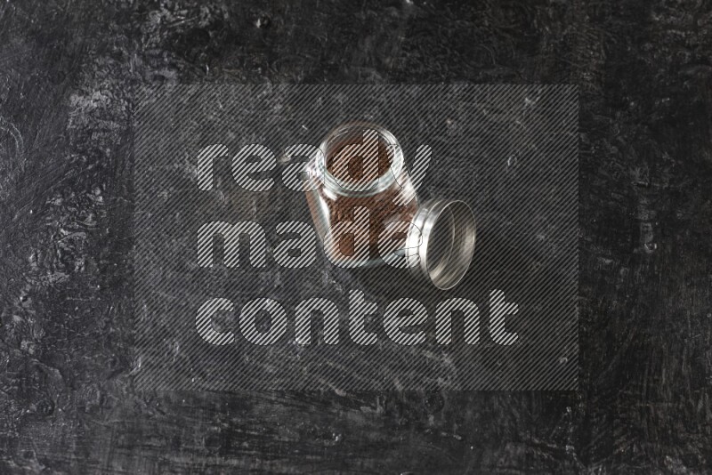 وعاء بهارات زجاجي ممتلئ ببودرة القرنفل على أرضية سوداء