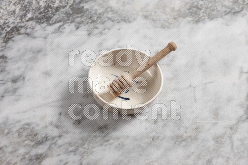 Multicolored pottery bowl with wooden honey dipper in it on grey marble background