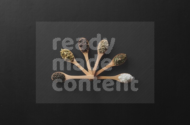 wooden spoons filled with white peppers, cloves, cardamom, salt, black peppers and basil on black flooring