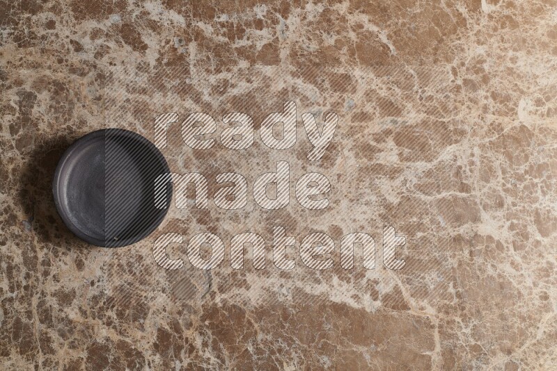 A black pottery bowl on beige marble background