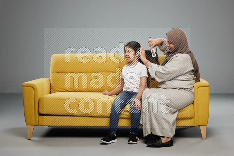 A mother sitting styling hair for her daughter on gray background