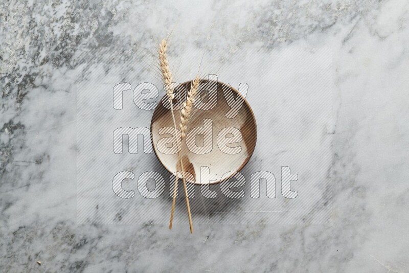 Wheat stalks on multicolored pottery plate on grey marble background