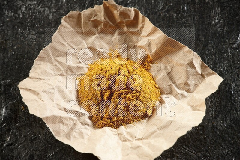 Turmeric powder in a crumpled piece of paper on textured black flooring