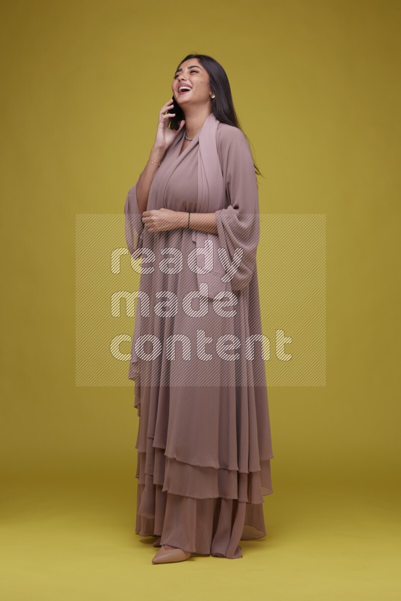 A woman Calling on a Yellow Background wearing Brown Abaya