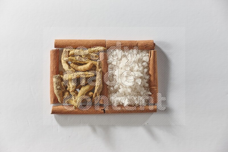 مربعان من أعواد القرفة ممتلئان بأصابع الكركم والملح الأبيض علي خلفية بيضاء