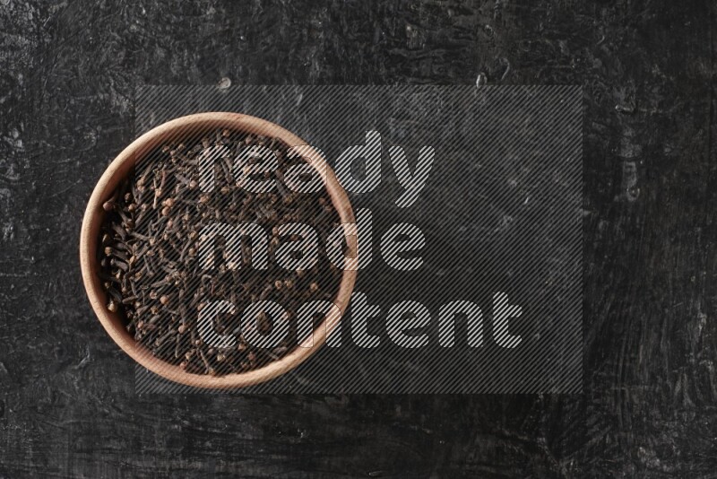 A wooden bowl full of cloves on a black flooring