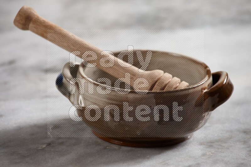Multicolored pottery bowl with wooden honey dipper in it on grey marble background