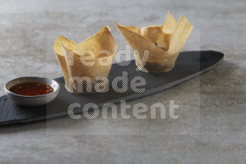 wonton cups with soy sauce ramkin on oval slate on grey textured counter top