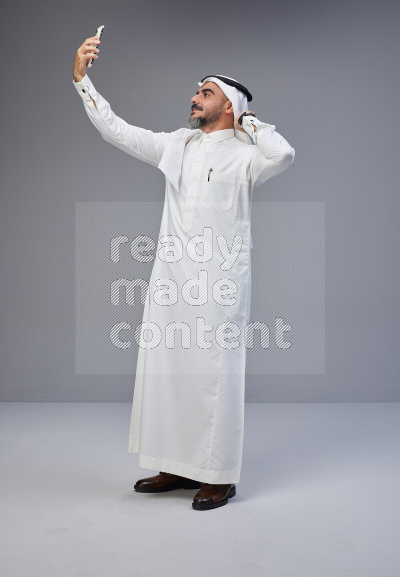 Saudi man Wearing Thob and white Shomag standing taking selfie on Gray background