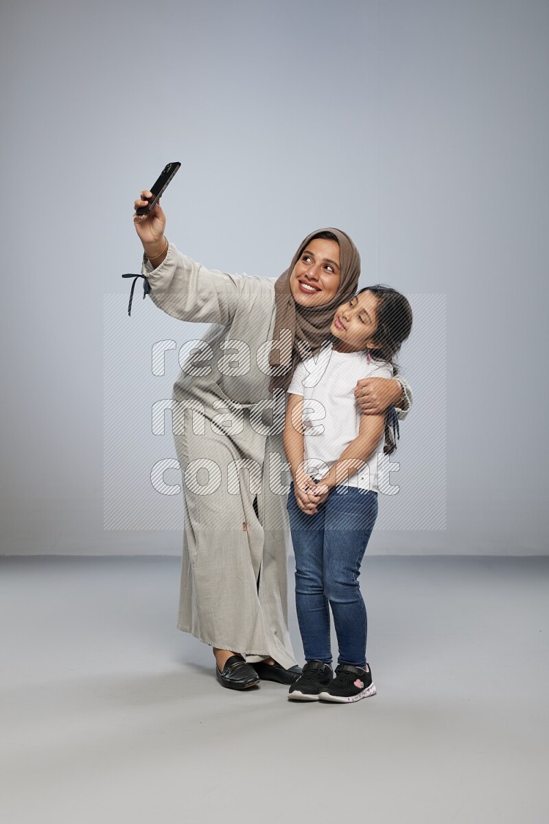 A girl standing taking selfie with her mother on gray background