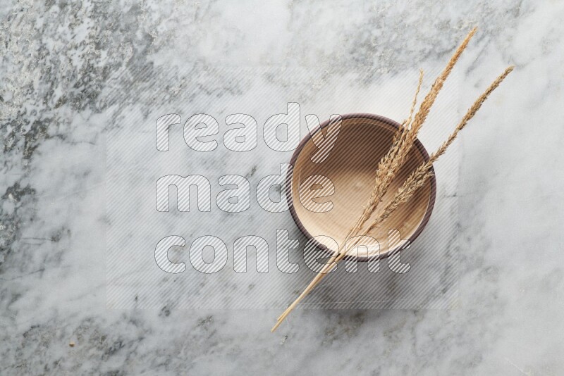 Wheat stalks on beige pottery oven bowl on grey marble background
