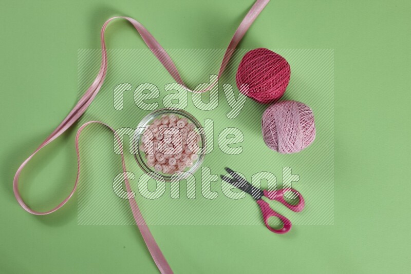 A pink collection of sewing and tailoring tools arranged on a green background