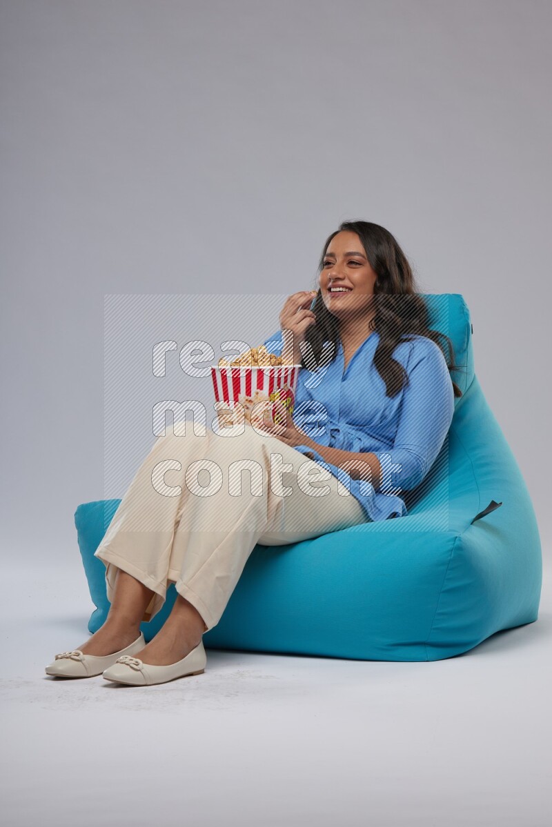 A woman sitting on a blue beanbag and eating popcorn
