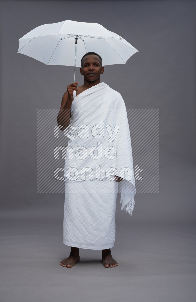 A man wearing Ehram Standing holding umbrella on gray background