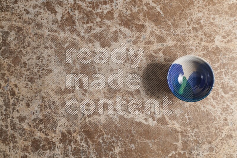 A multicolored pottery bowl on beige marble background