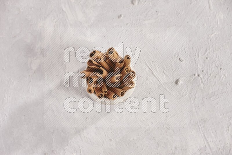 Cinnamon sticks in a beige bowl and more sticks beside it on white background