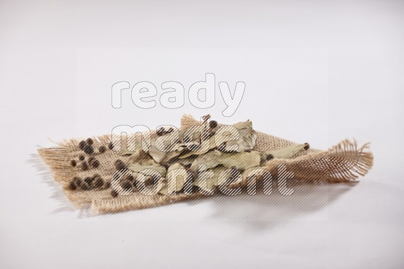 أوراق الغار المجففة مع حبوب البهار الحلو علي قطعة من قماش الخيش علي خلفية بيضاء