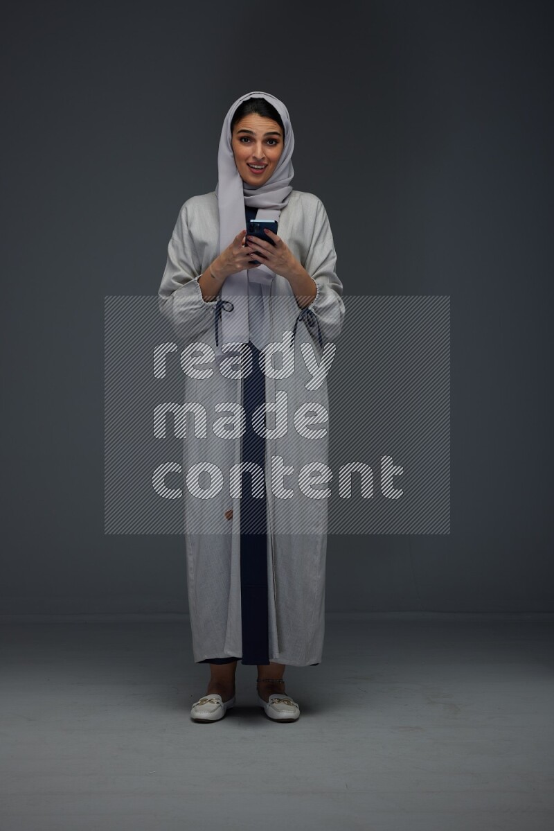 A Saudi woman Texting wearing Grey Abaya on a grey background
