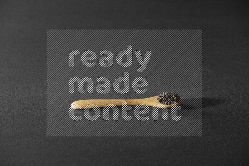 A wooden spoon full of black pepper on a black flooring