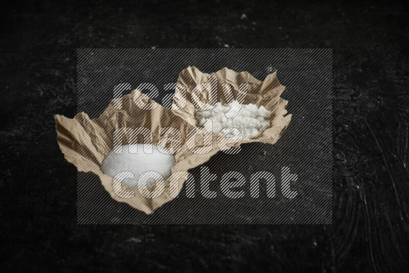 A crumpled piece of paper full of white salt on black background