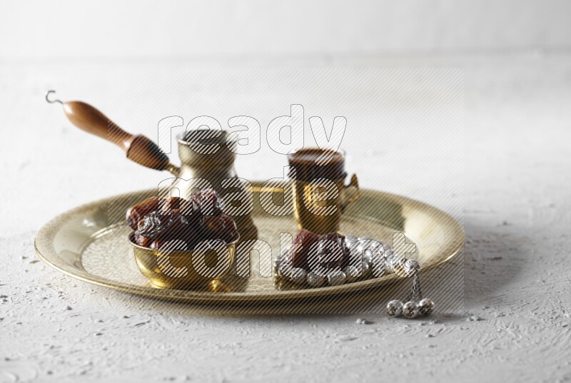 Dates in a metal bowl with coffee and prayer beads on a tray in a light setup