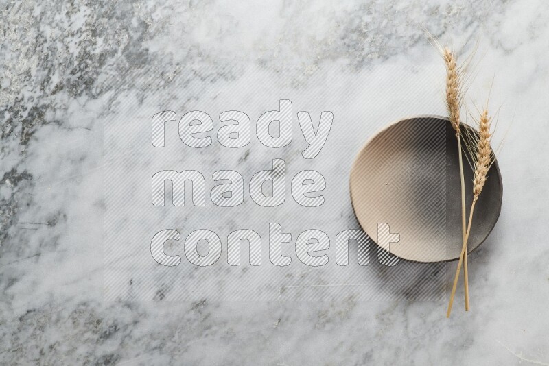 Wheat stalks on multicolored pottery plate on grey marble background
