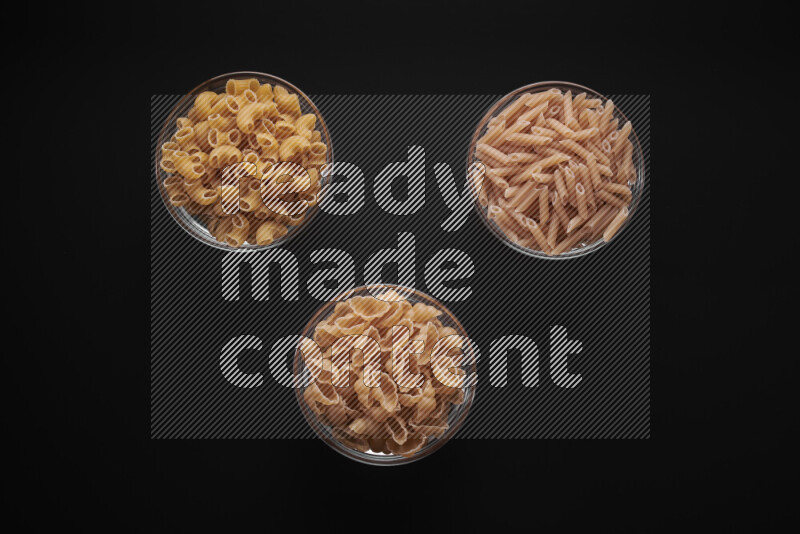 Different pasta types in glass bowls on black background