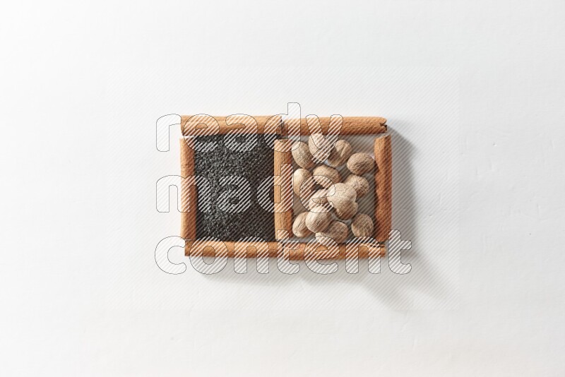 مربعان من أعواد القرفة ممتلئان بحبة البركة السوداء وجوزة الطيب علي خلفية بيضاء