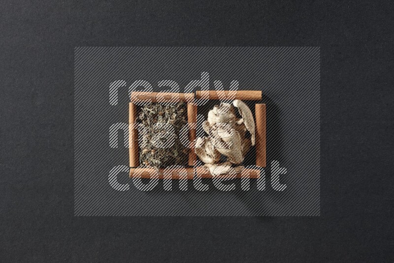 مربعان من أعواد القرفة ممتلئان بالزنجبيل المجفف والريحان المجفف علي خلفية سوداء