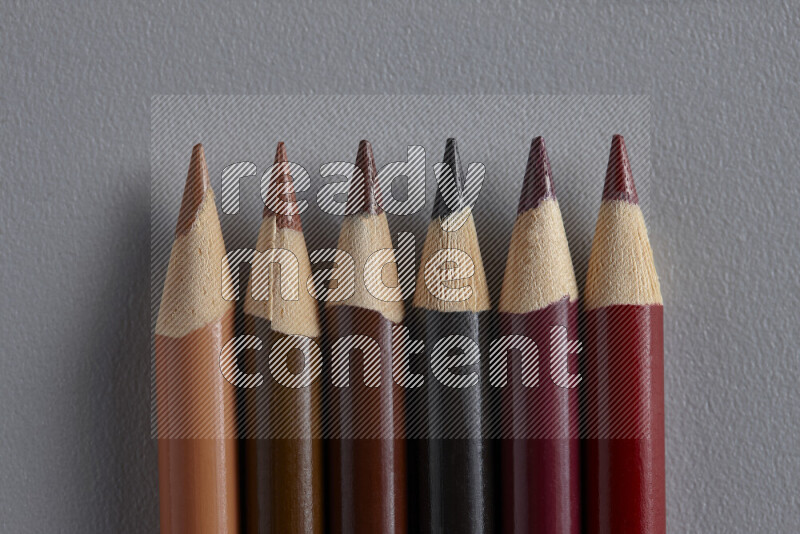A collection of colored pencils arranged showcasing a gradient of brown hues on grey background
