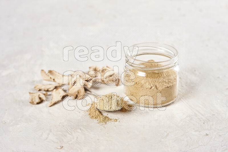 A glass jar full of ground ginger powder on white background