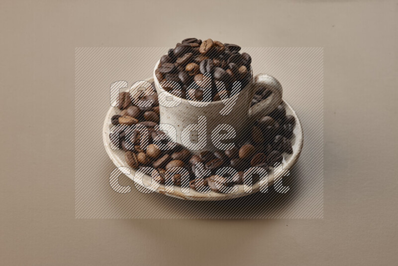 A beige pottery cup full of roasted coffee beans on beige background