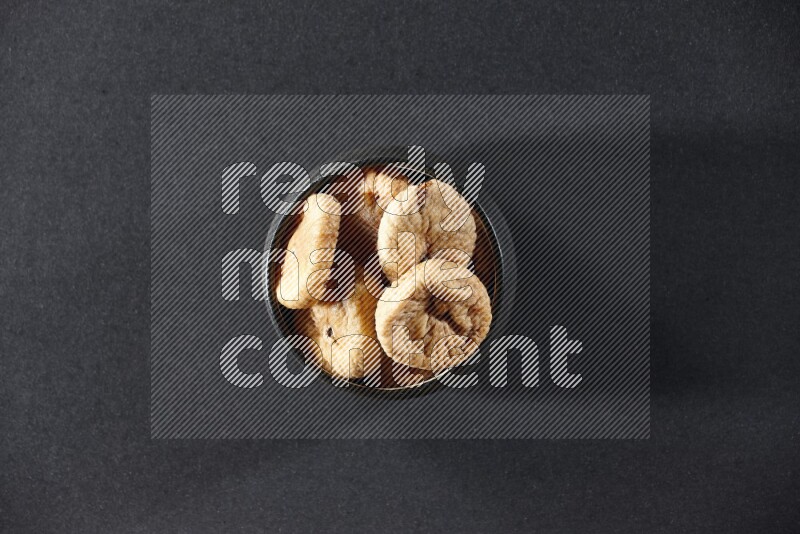 A black pottery bowl full of dried figs on a black background in different angles