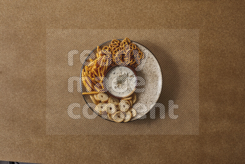 Assorted snacks on a pottery plate with a dipping on brown background