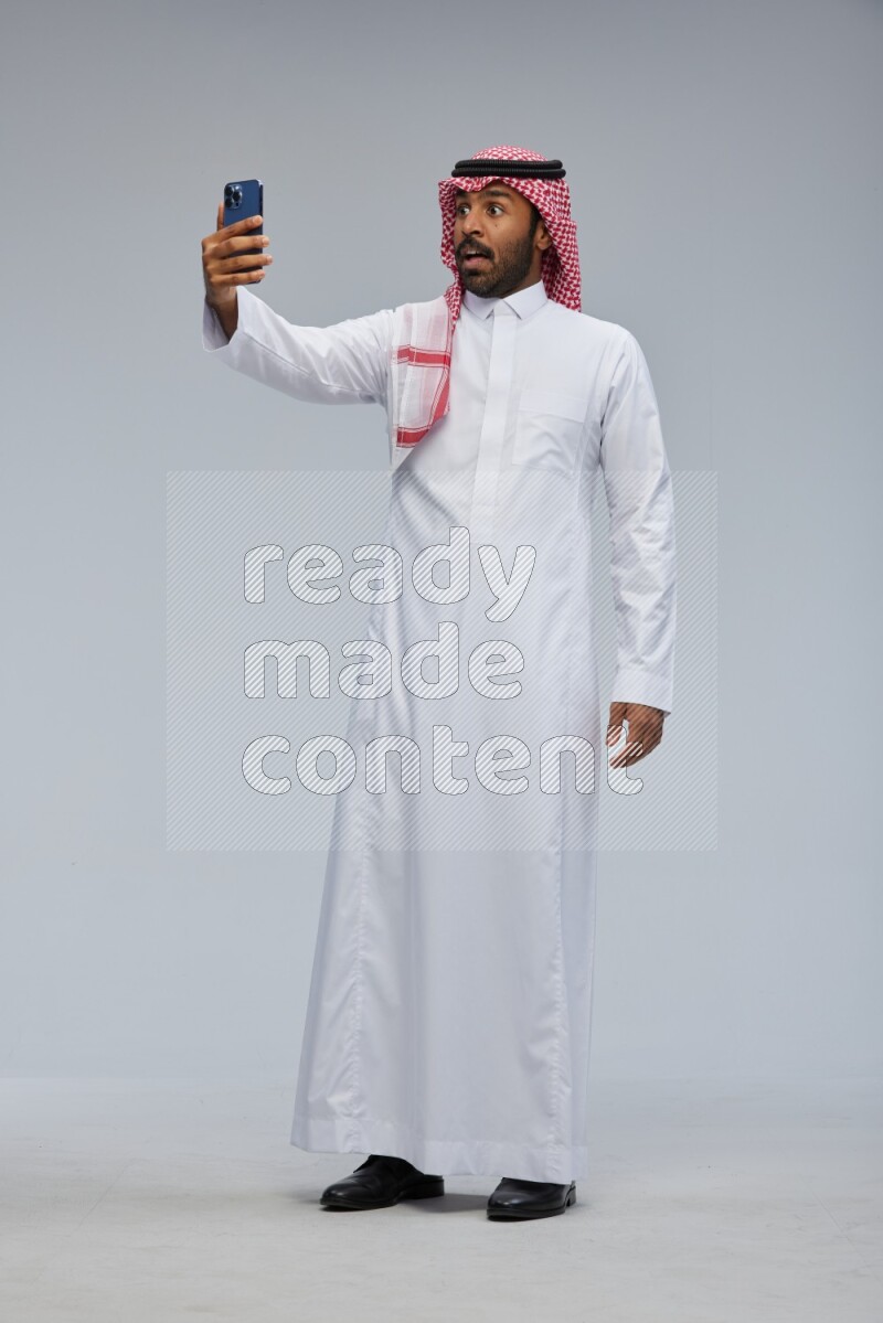 Saudi man Wearing Thob and shomag standing taking selfie on Gray background
