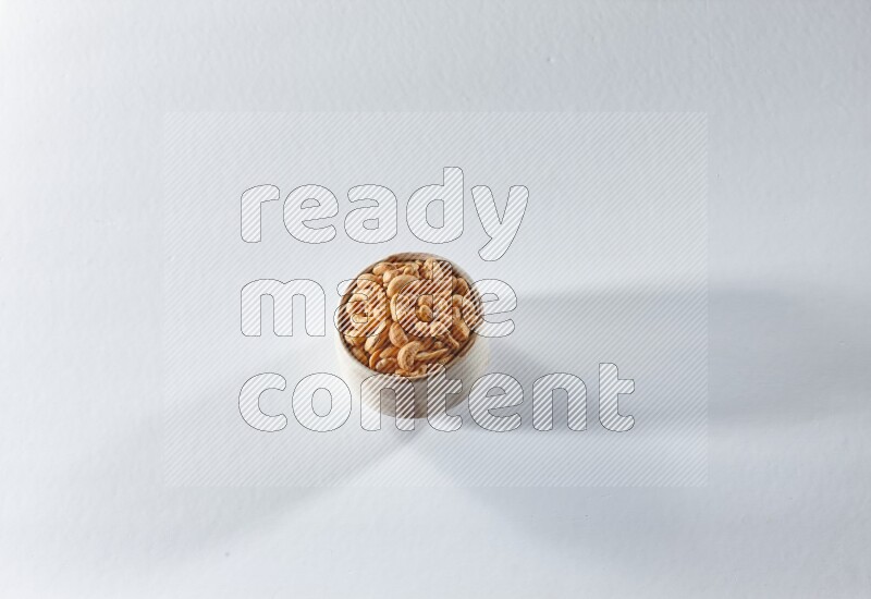 A beige ceramic bowl full of cashews on a white background in different angles