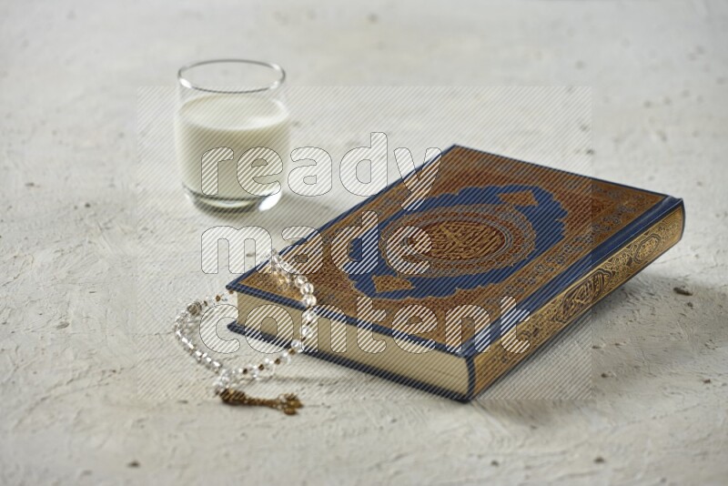Quran with dates, prayer beads and different drinks all placed on textured white background