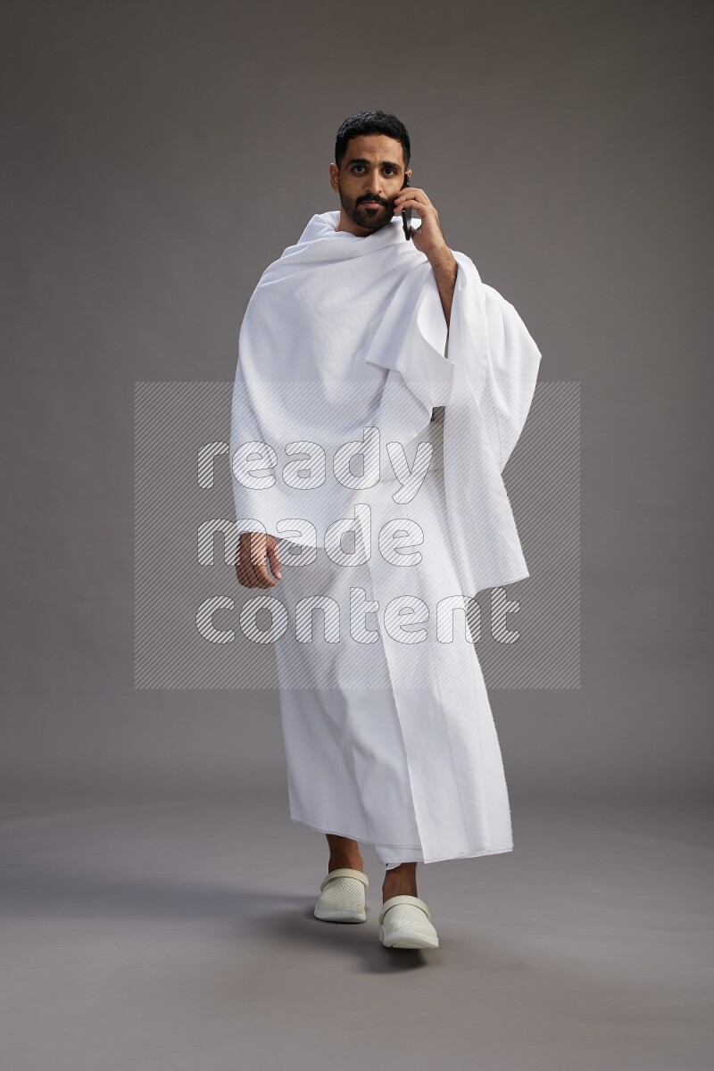 A man wearing Ehram Standing talking on phone on gray background