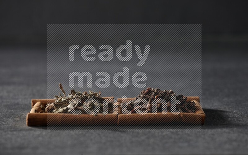 2 squares of cinnamon sticks full of cloves and dried basil on black flooring