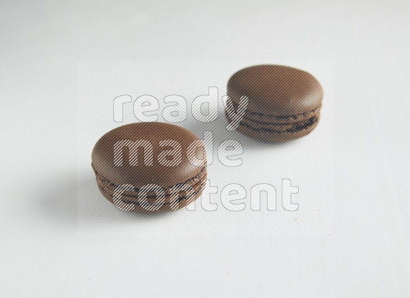 45º Shot of two Brown Dark Chocolate macarons on white background