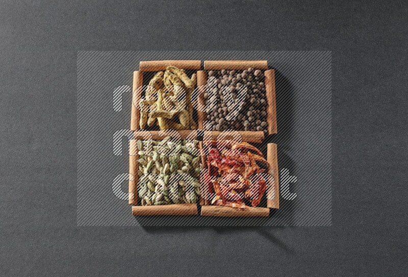 4 squares of cinnamon sticks full of cardamom, dried red chilis, allspice and turmeric fingers on black flooring