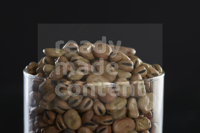 Fava beans in a glass jar on black background